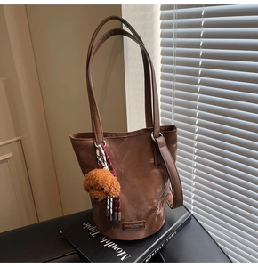 Detailed view of a brown faux leather bucket bag with a plush dog charm and braided cord