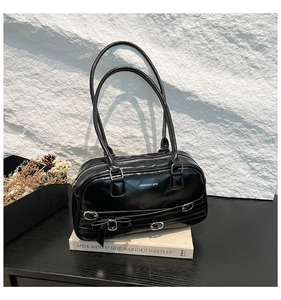 Détail du sac porté épaule noir brillant avec sangles décoratives et nœud sur des livres