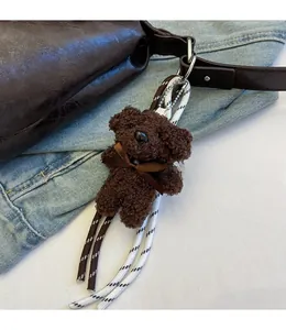 Detail of a dark brown plush bear charm with a silk bow on a leather bucket bag