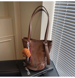 Detail of a brown bucket bag with plush bear charm and metallic buckle accents
