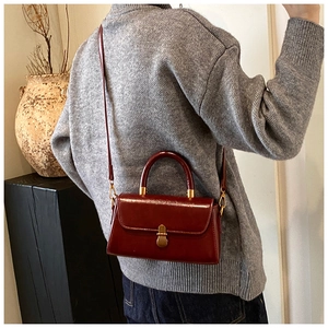 Detail of vintage burgundy leather crossbody bag with metallic clasp worn by a model