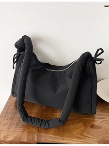 Quilted black nylon shoulder bag with bow accents and padded handle on wood surface