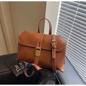 Detail of vintage brown leather bag with gold buckle and white stitching on black surface