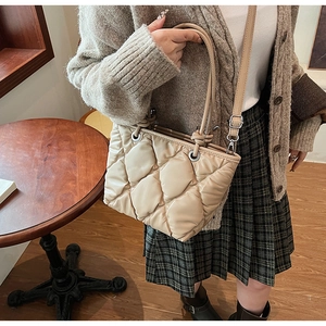 Détail du sac seau matelassé beige montrant les surpiqûres en losange et les rivets
