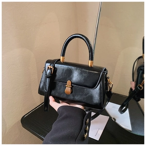 Close-up of black glossy leather handbag with vintage bronze clasp and mirror reflection
