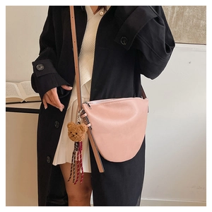 Detail of pink crescent crossbody bag with adjustable strap and bear charm accessory
