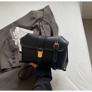 Detail of a black leather crossbody bag with white stitching and gold hardware on a desk