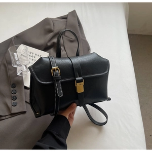 Detail of matte black handbag featuring white contrast stitching and gold metal buckles