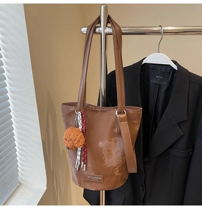 Brown leather bucket bag detail with teddy bear charm and brand logo plate hanging on a rack