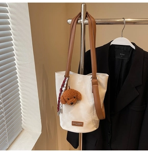 Close-up of cream bucket bag with brown leather straps and cute plush dog charm