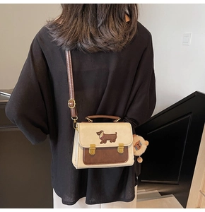 Model wearing a two-tone square crossbody bag with dachshund embroidery and plush charm