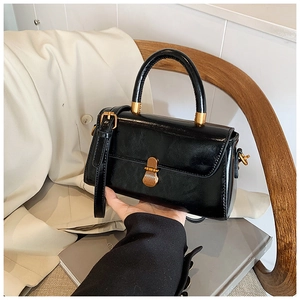 Detail of a black crossbody bag with gold hardware and a top handle on a beige trench coat