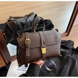 Detail of vintage messenger bag with white stitching and gold metal lock on rich leather