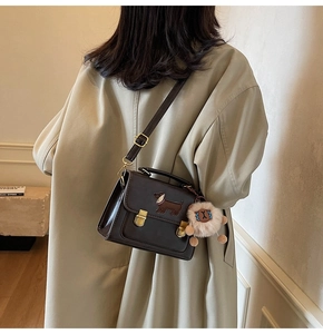 Detail of dark brown leather crossbody bag with dachshund embroidery and white plush charm