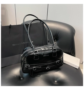 Détail d'un sac d'épaule en cuir verni noir avec nœud et boucles argentées sur un siège