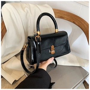 Detailed view of a black glossy patent leather square bag with gold metal buckle