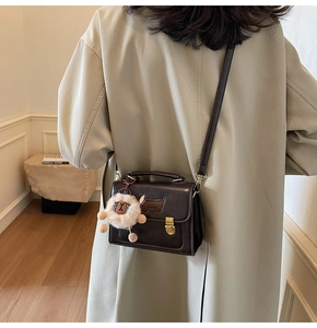 Detail of dark brown leather crossbody bag with dog stitching and cute sheep charm