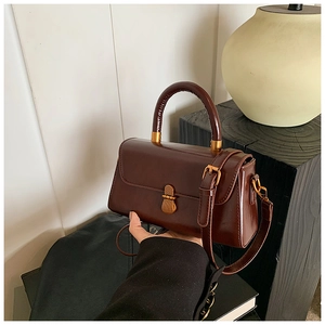 Detail of vintage dark brown faux leather bag with gold buckle and top handle grip