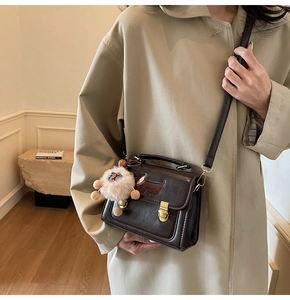 Detail of vintage dark brown crossbody bag with plush charm on a beige trench coat