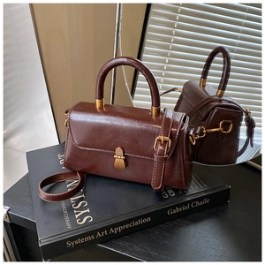 Detail view of vintage brown leather square bag with gold buckle on a black book