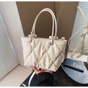 Gros plan d'un sac seau matelassé crème avec texture rembourrée et détail de poignée nouée