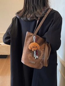 Vintage dark brown bucket bag with a plush puppy charm and textured faux leather finish