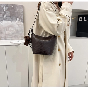 Detail of vintage brown bucket bag featuring pleated leather and a plush bear pendant