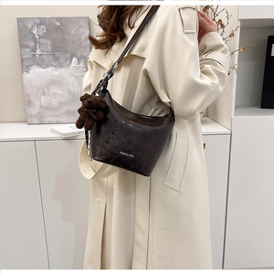 Close-up of vintage brown hobo bag with teddy bear charm and silk scarf on beige trench coat