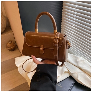 Detail view of a vintage brown leather handbag with metallic buckle and sturdy top handle