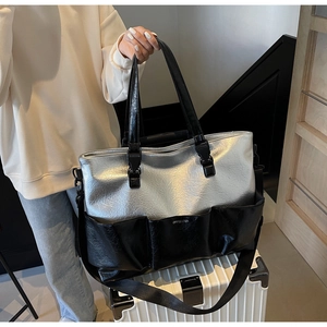 Detail of silver metallic tote bag with black accents and wide shoulder strap on luggage