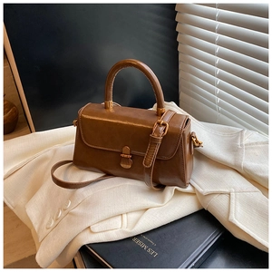 Detail view of a vintage dark brown leather crossbody bag with bronze hardware on a blazer