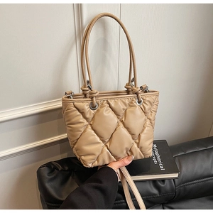 Détail du sac seau matelassé beige avec texture souple et œillets sur un canapé noir