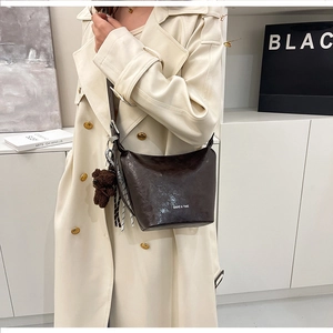 Detail of dark brown leather bucket bag featuring a plush bear charm and striped scarf