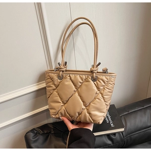 Gros plan d'un sac cabas matelassé beige avec surpiqûres losanges et œillets en métal