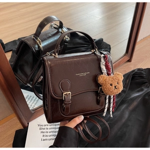 Detail of dark brown vintage faux leather handbag with golden buckles and teddy bear charm