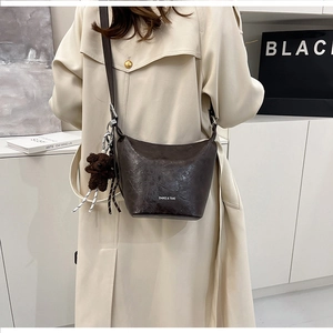 Detail of dark brown bucket bag with plush bear charm and adjustable shoulder strap