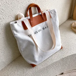 Close-up of beige canvas tote bag with brown leather handle and wide shoulder strap