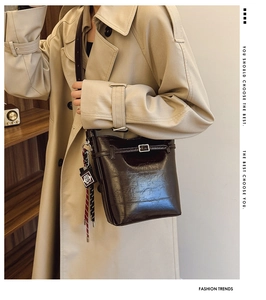 Detail of glossy brown leather bucket bag with decorative buckle and woven strap pendant