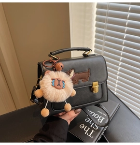 Close-up of black leather crossbody bag with dog embroidery and large plush pompom charm
