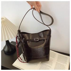Detail of coffee brown leather bucket bag with silver buckle and braided charm on desk
