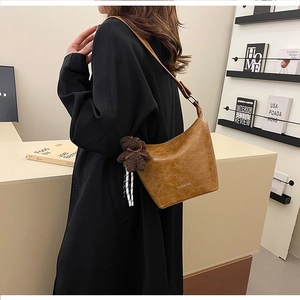 Detail of a brown pleated crescent bag with a plush bear charm on a black coat outfit