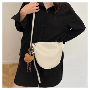 Model wearing a white half-moon crossbody bag with a plush bear charm and silver zipper