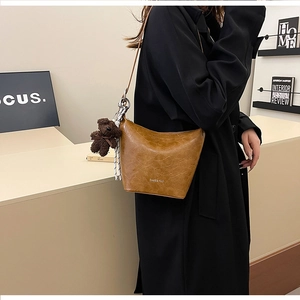 Detail of vintage brown bucket bag with plush bear charm worn over a black winter coat