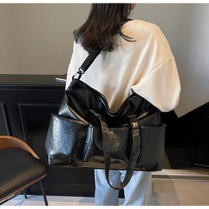 Close-up of black glossy textured tote bag featuring wide shoulder straps and side pockets