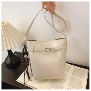 Detail of cream bucket bag with faux crocodile texture, silver buckle and woven charm