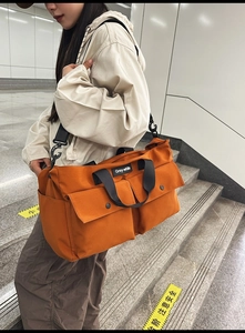 Detail of orange canvas tote bag with front pockets and adjustable strap shown on model