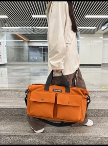 Outdoor shot of the orange canvas tote bag showing dual front pockets and shoulder strap
