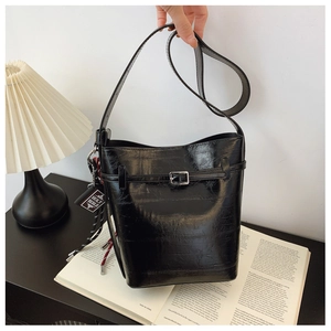 Detail of glossy black patent leather bucket bag with silver buckle and book charm
