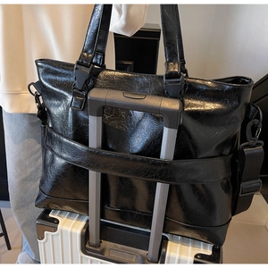 Detail of black textured tote bag with luggage strap fixed on a white suitcase handle