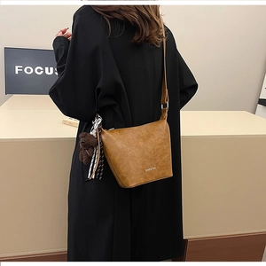 Brown vintage bucket bag worn as crossbody with cute bear charm and silk ribbon detail